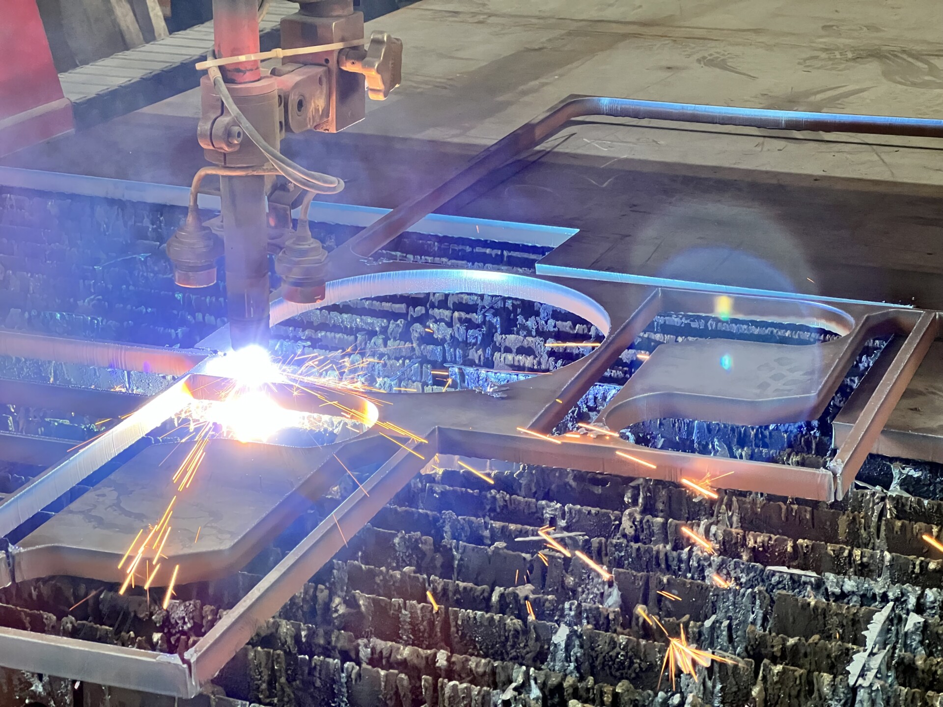 A plasma cutting machine using a bright plasma arc to burn precise outlines and intricate designs into a metal sheet.